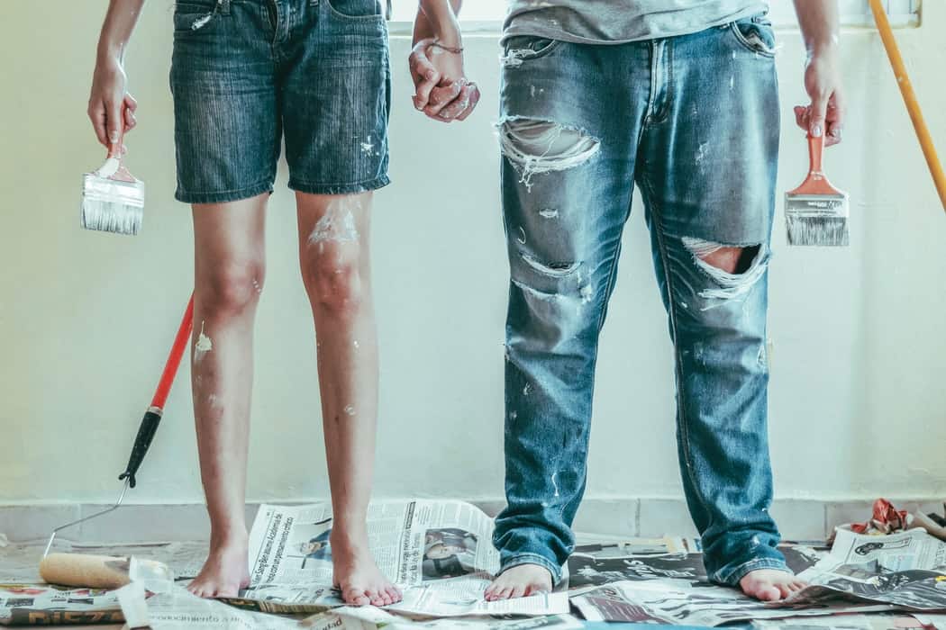 couple holding hands and paint brushes in home